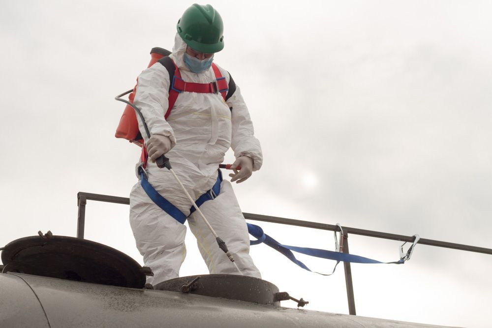 A Man In A Protective Suit Is Spraying Something On A Pipe — Eureka Water & Filtration In Mount St John, QLD