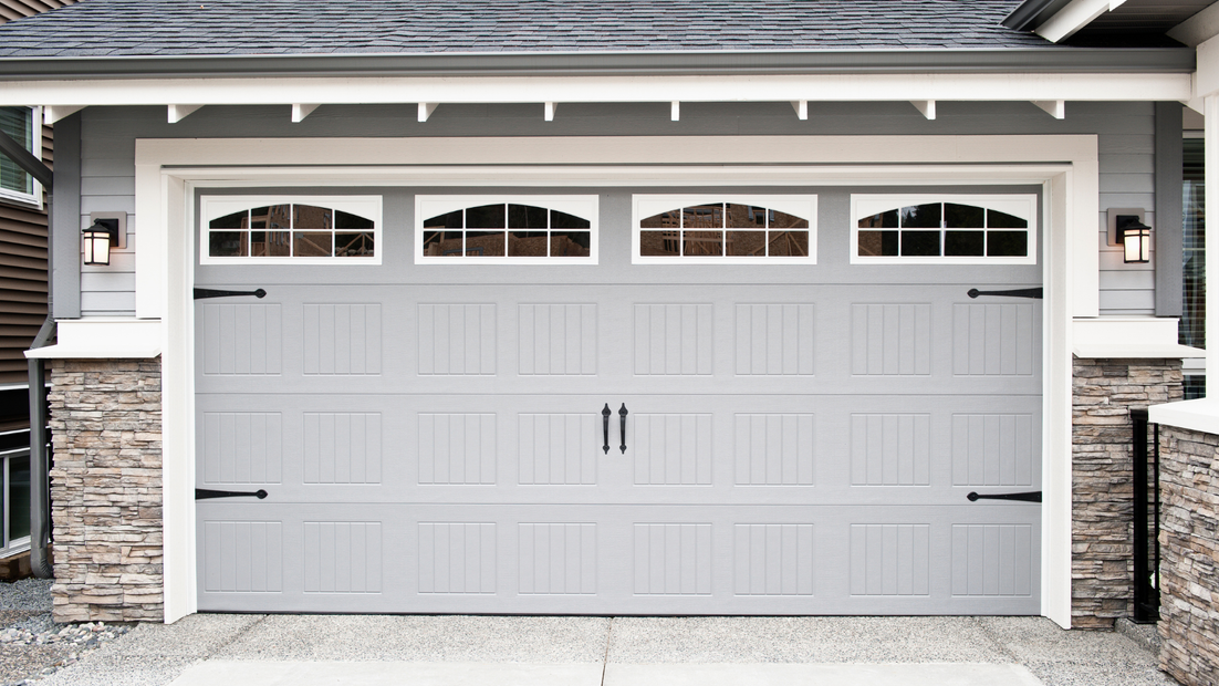 Gray garage door with windows and black hardware, framed by stone and a light gray facade.