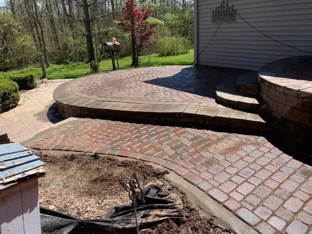 A wheelbarrow is sitting next to a pile of bricks in front of a house. brick paver patio 