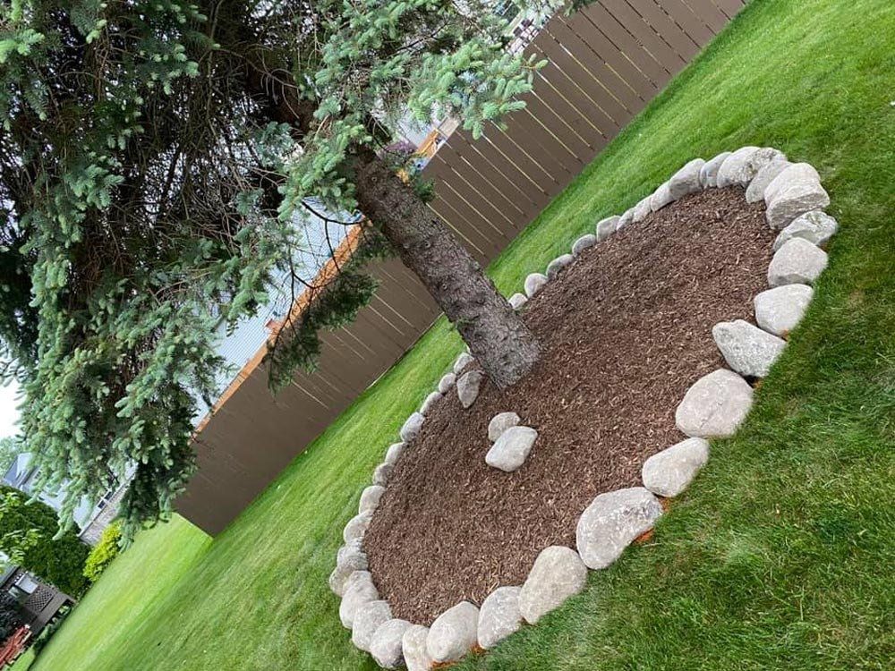 A wooden deck is sitting under a tree in the backyard of a house. mulch