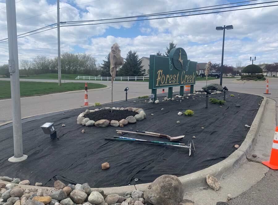 A wooden barrel is sitting in a planter filled with red mulch. mulch