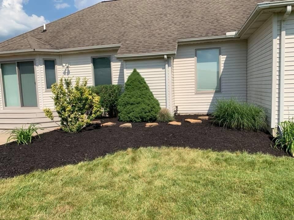 A white fence is surrounded by trees and bushes in a yard. mulch