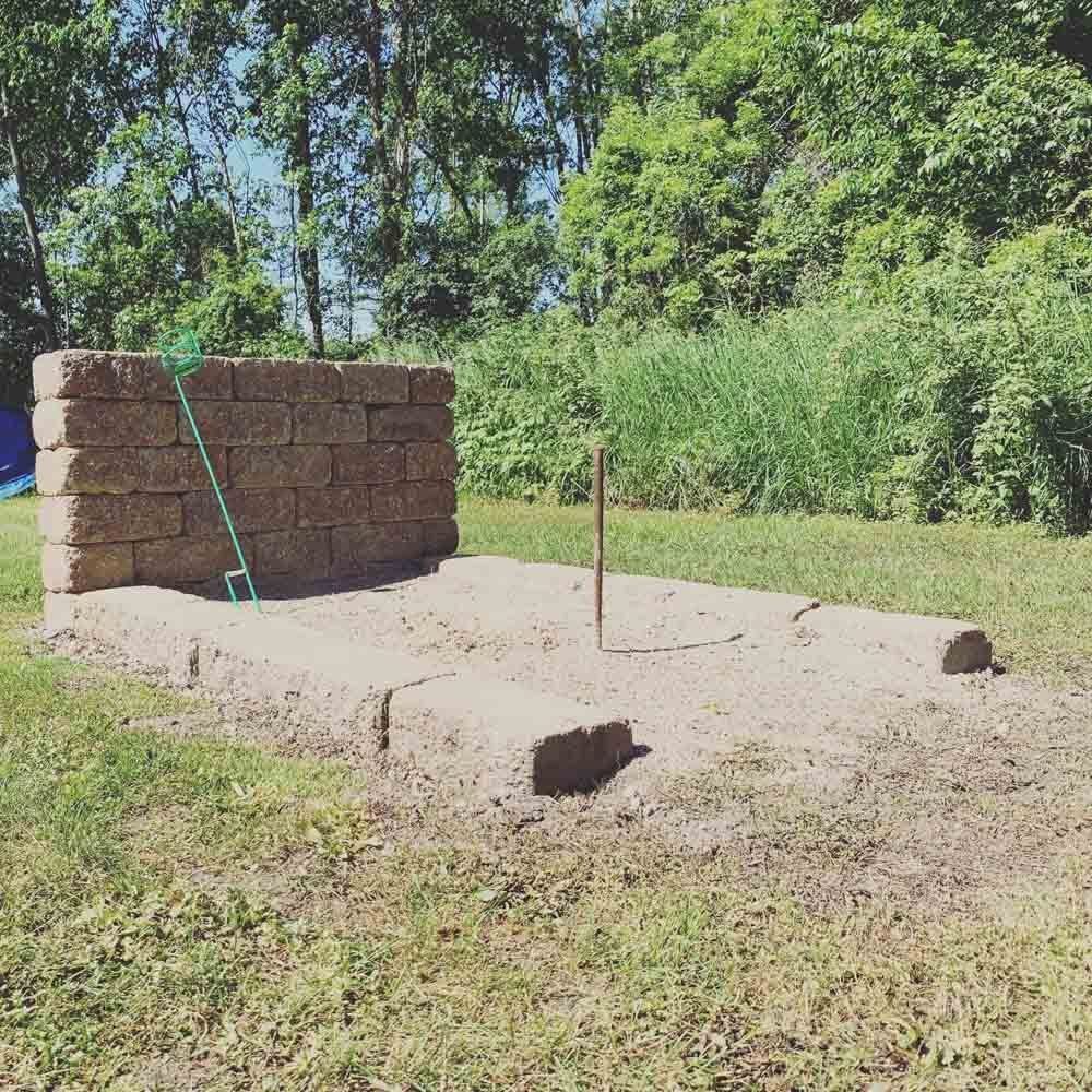 A person is laying on a large rock in the grass. fire pit