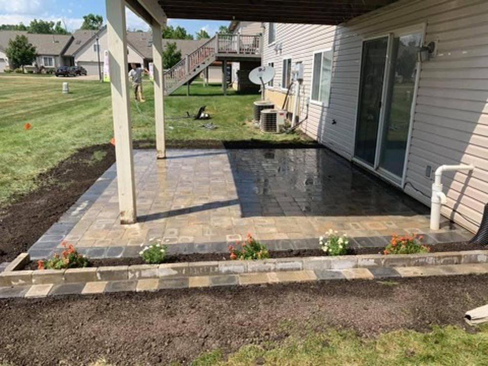 Two men are working on a patio with a wheelbarrow. brick paver patio