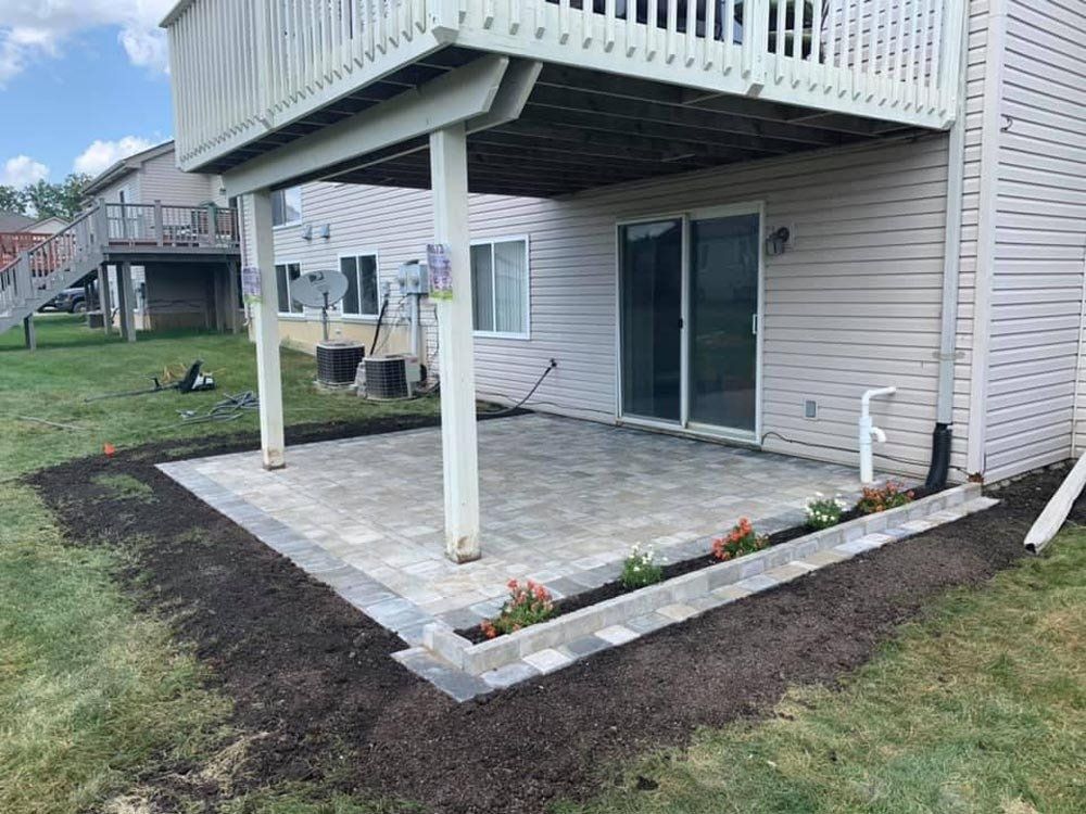A patio under a deck is being built in the backyard of a house. brick paver patio 
