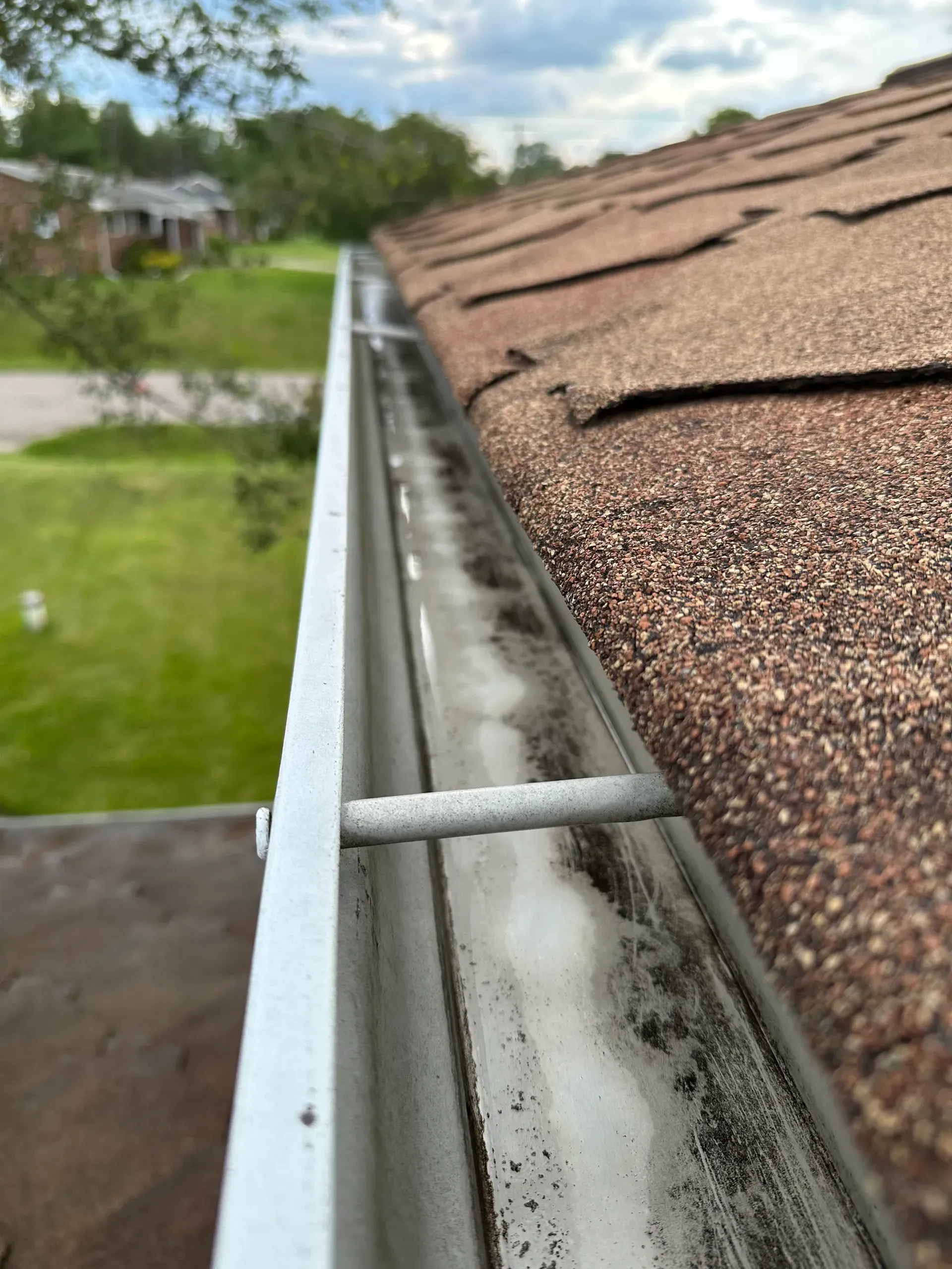 A close-up view of a dirty gutters on a brown roof, with debris visible inside.