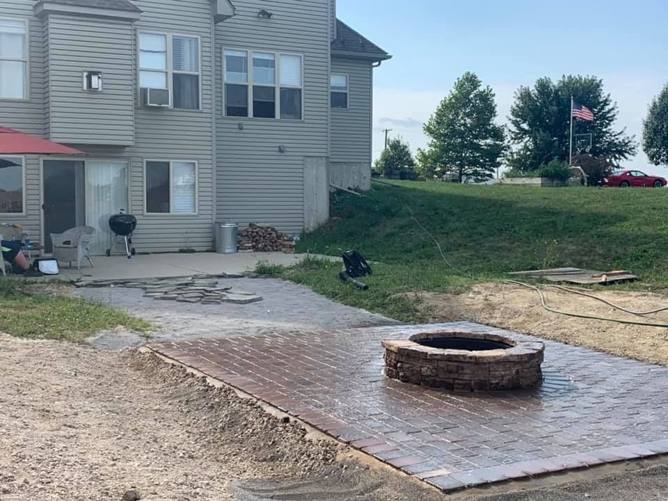 A fire pit is in the middle of a patio in front of a house.