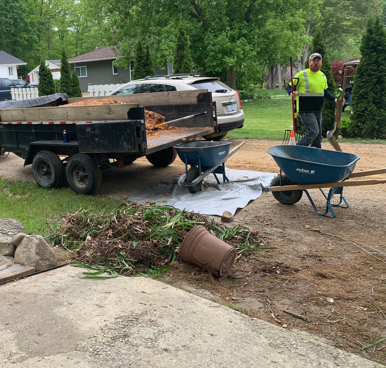 A man is standing next to a wheelbarrow and a dump truck. mulch install