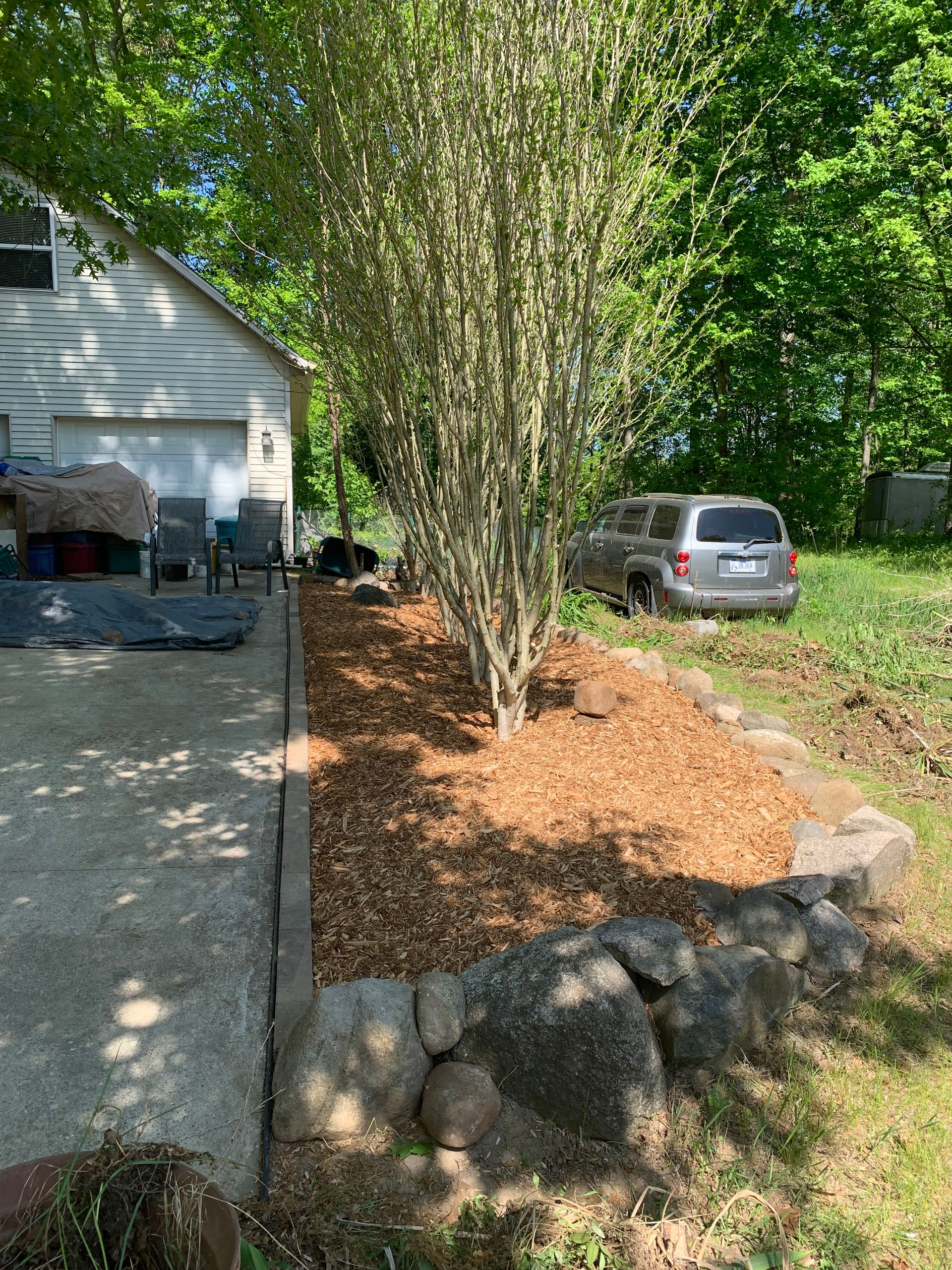 A car is parked in a driveway next to a house. mulch