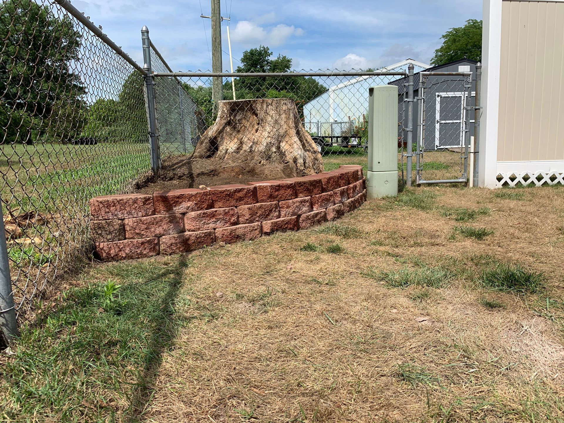 A large tree stump is sitting in the middle of a yard next to a chain link fence. commercial paving