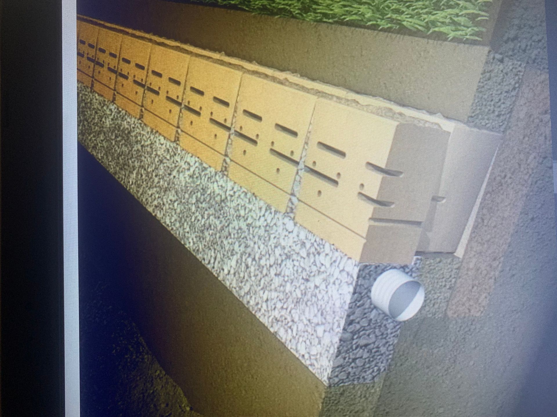 A brick wall is being built in a yard with trees in the background. hardscape