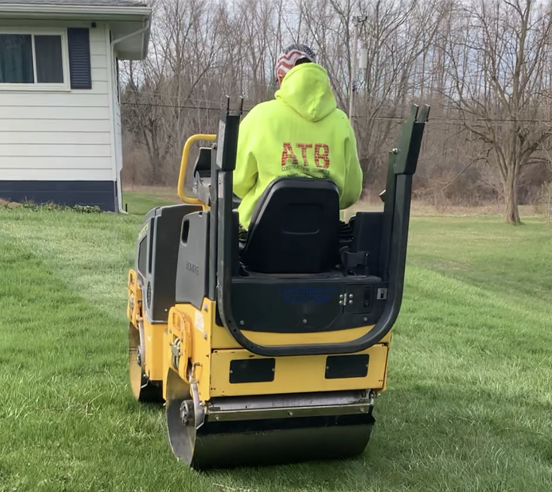 A man is blowing leaves in a yard with a backpack. landscape