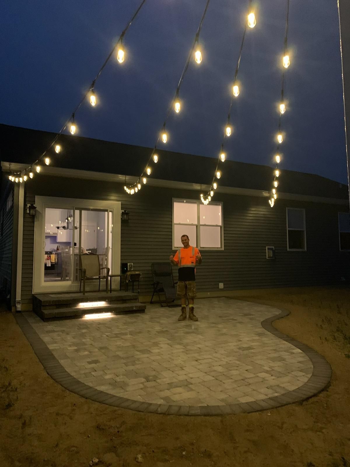 A man is standing on a patio in front of a house at night. Edison lighting