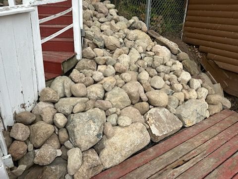 A pile of rocks sitting on top of a wooden deck next to a house. boulders