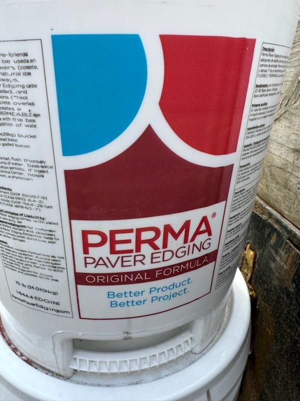 A man is kneeling on a patio with a wheelbarrow in the background. flagstone