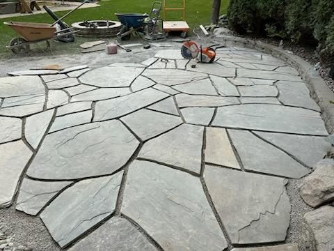 A man is kneeling on a patio with a wheelbarrow in the background. flagstone