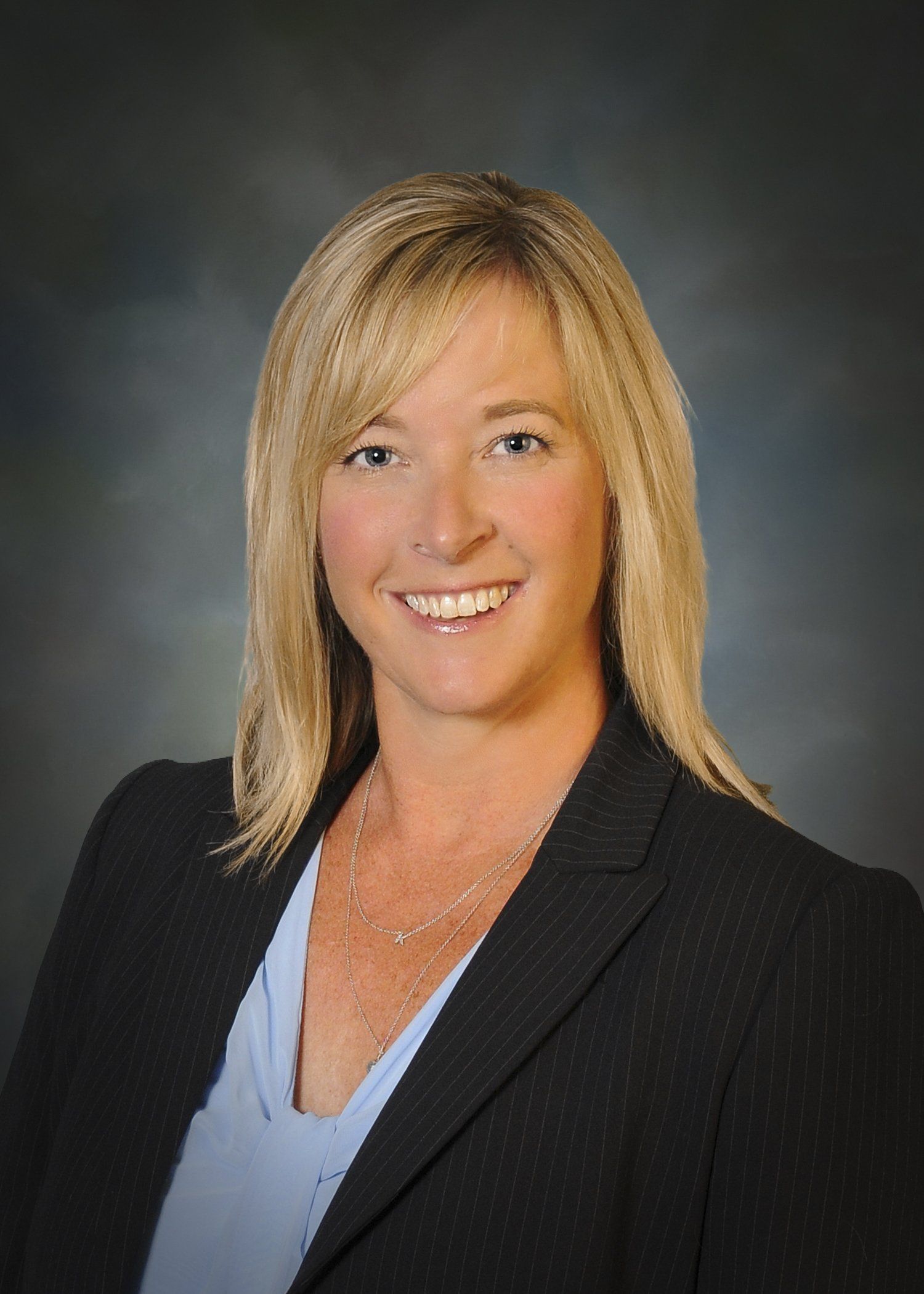 A woman in a suit and blue shirt is smiling for the camera.
