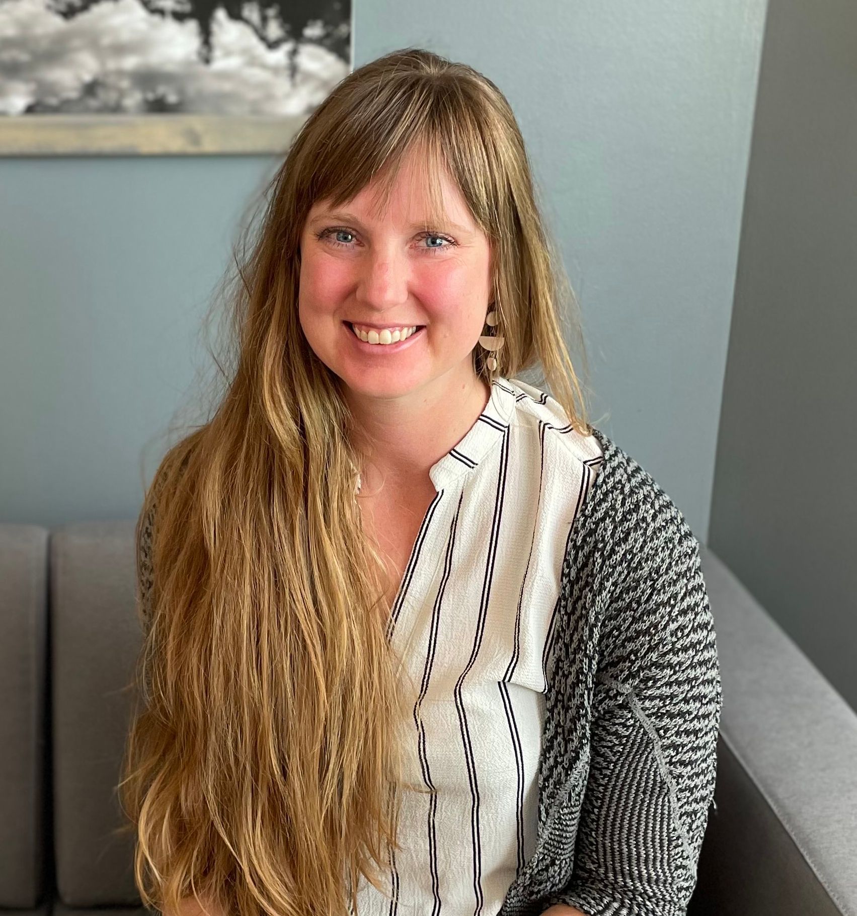 A woman with long hair is sitting on a couch and smiling.