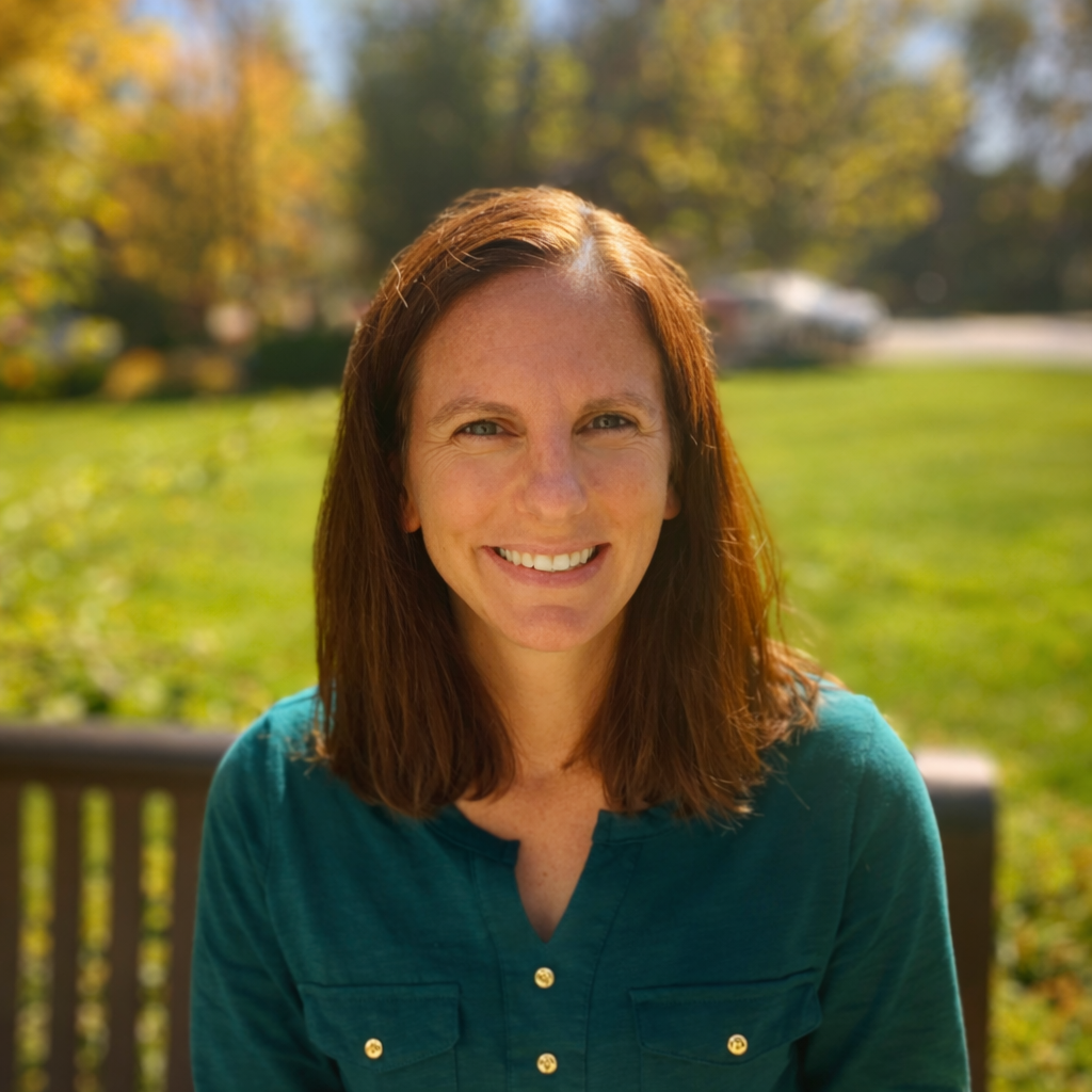 Woman in green shirt smiles outdoors, seated on a bench, with a green background.