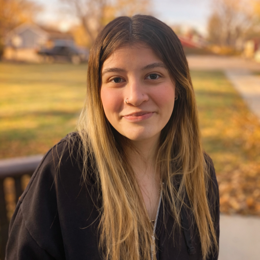 Woman with long hair smiles outside, blurred background of a house and greenery.