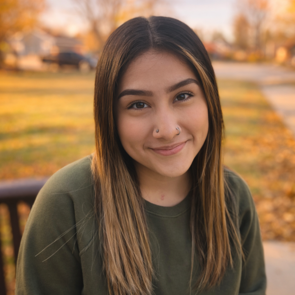 Woman with long hair smiles outdoors, wearing a green sweater.