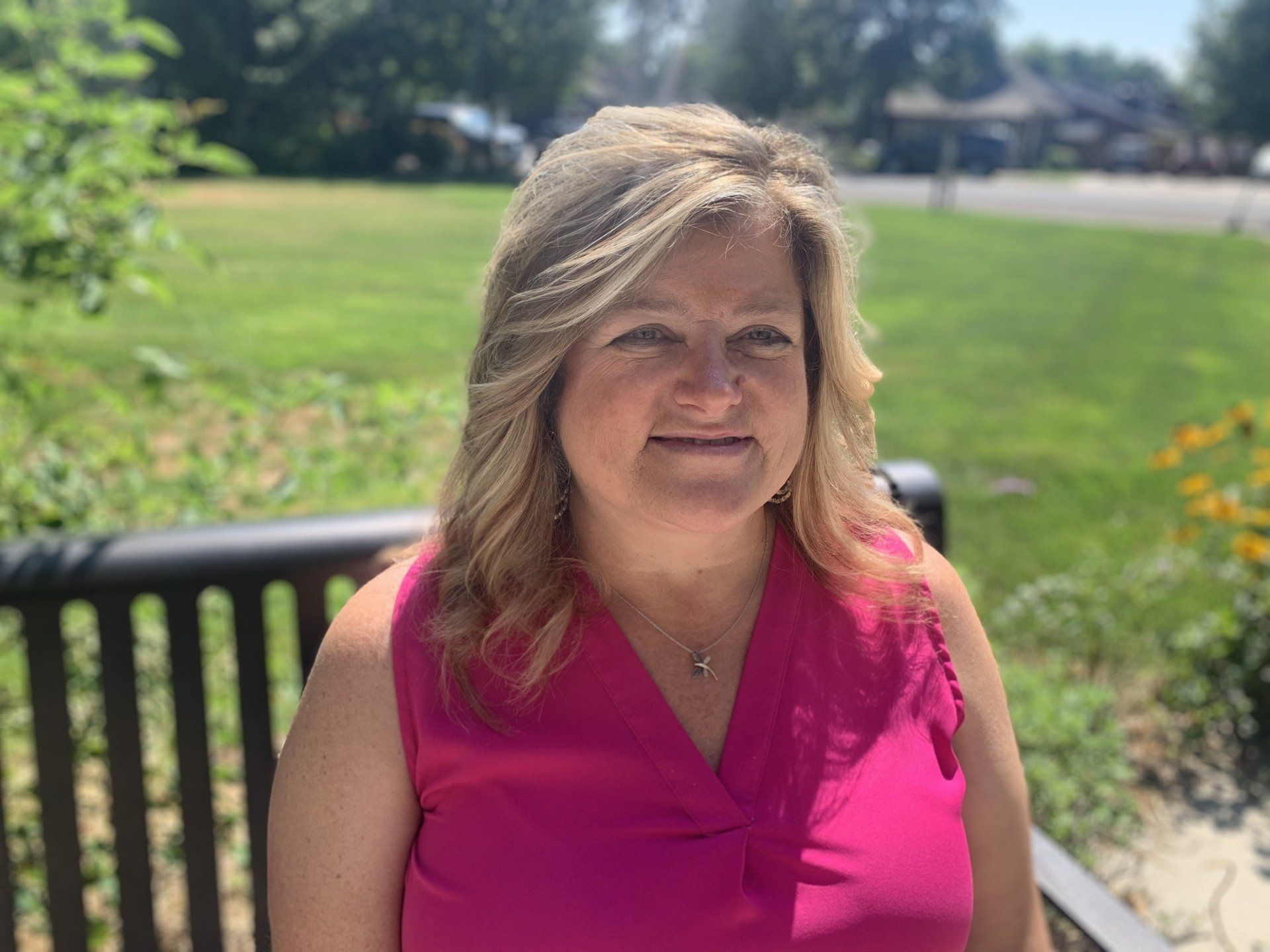 A woman in a pink shirt is sitting on a park bench.