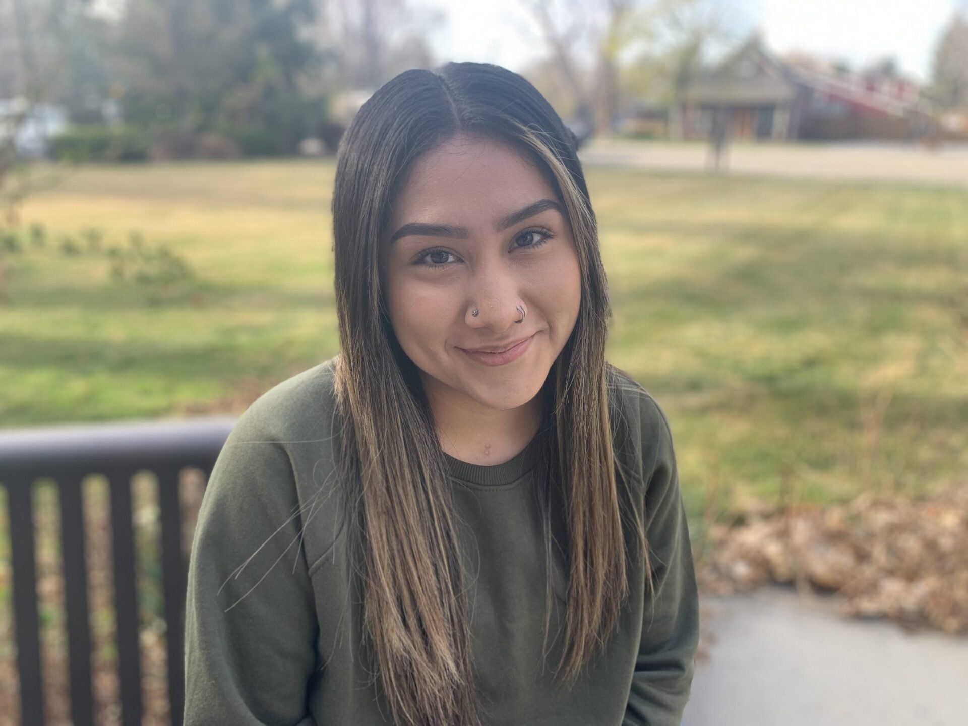 A woman is sitting on a bench in a park and smiling for the camera.