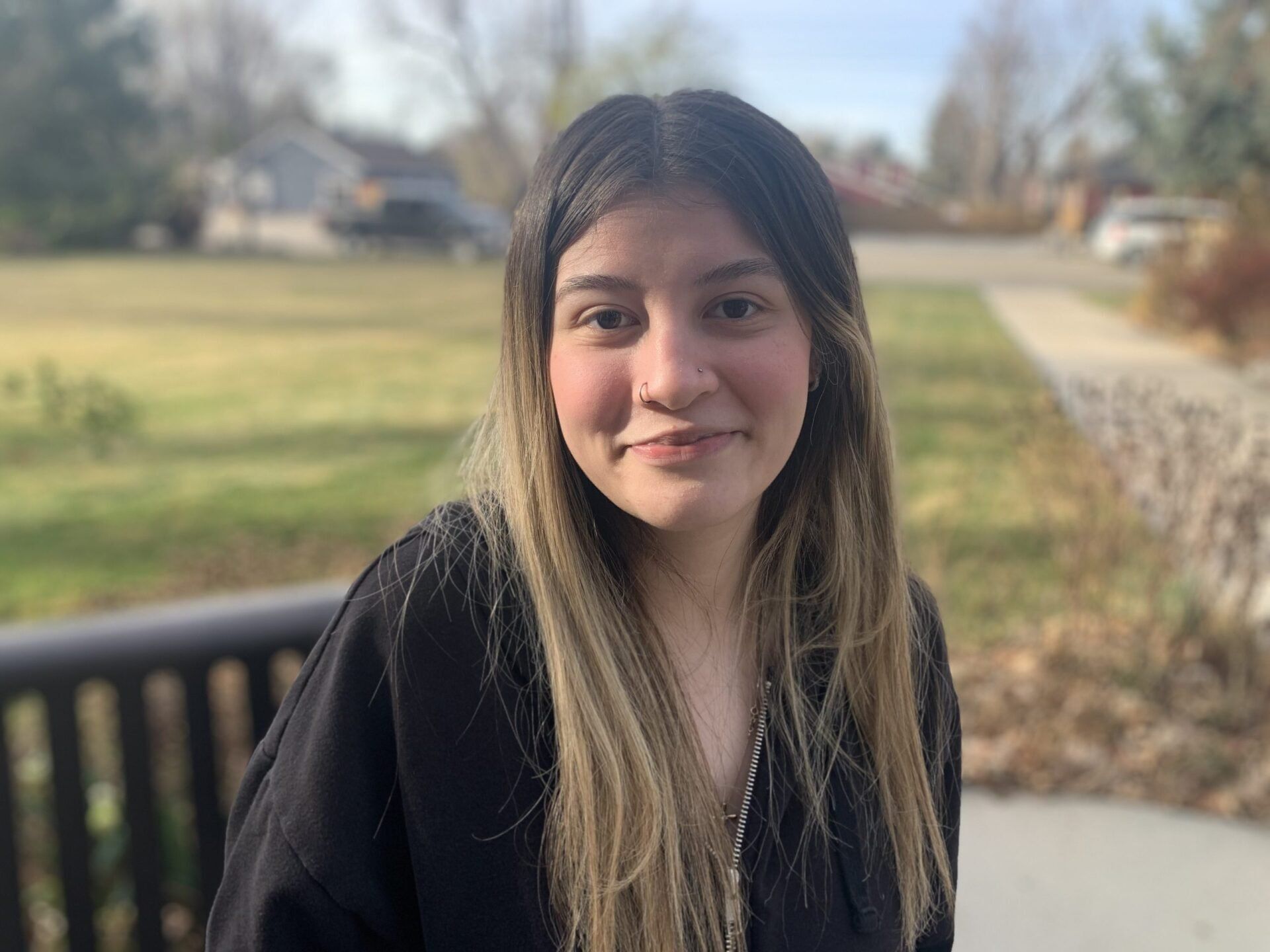 A young woman is standing in front of a park bench and smiling for the camera.