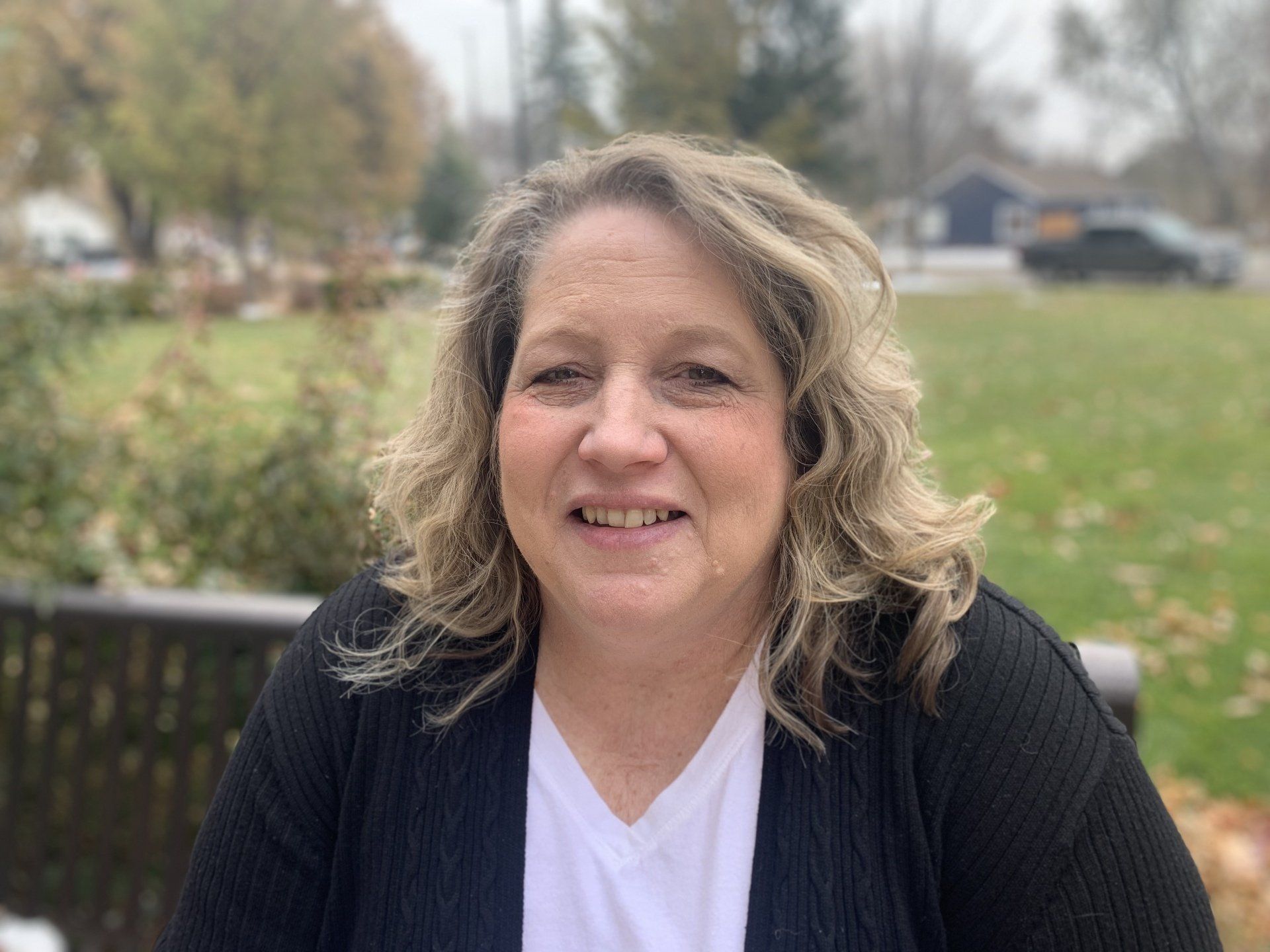 A woman is sitting on a bench in a park and smiling for the camera.