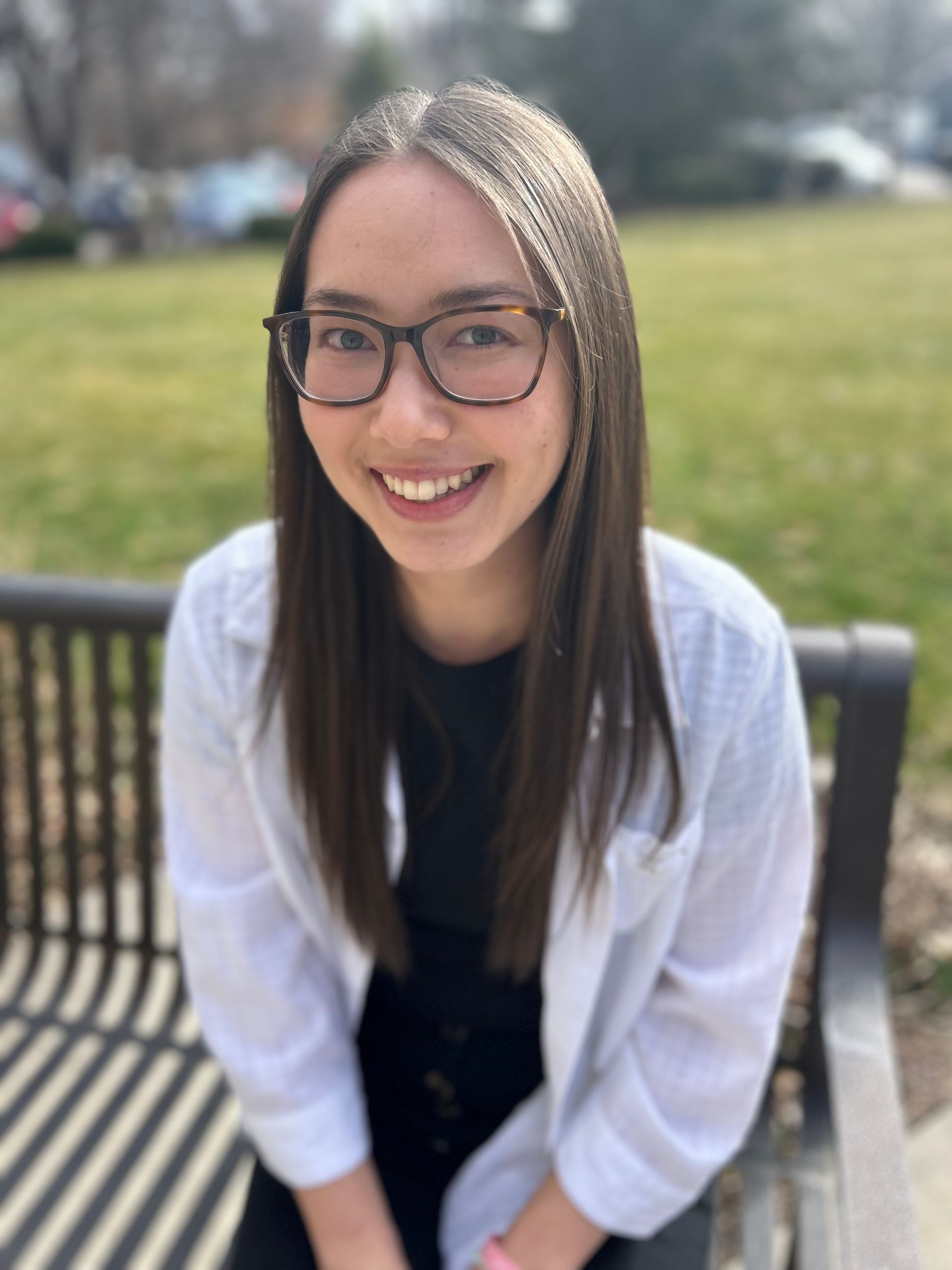 A woman wearing glasses and a white coat is sitting on a bench