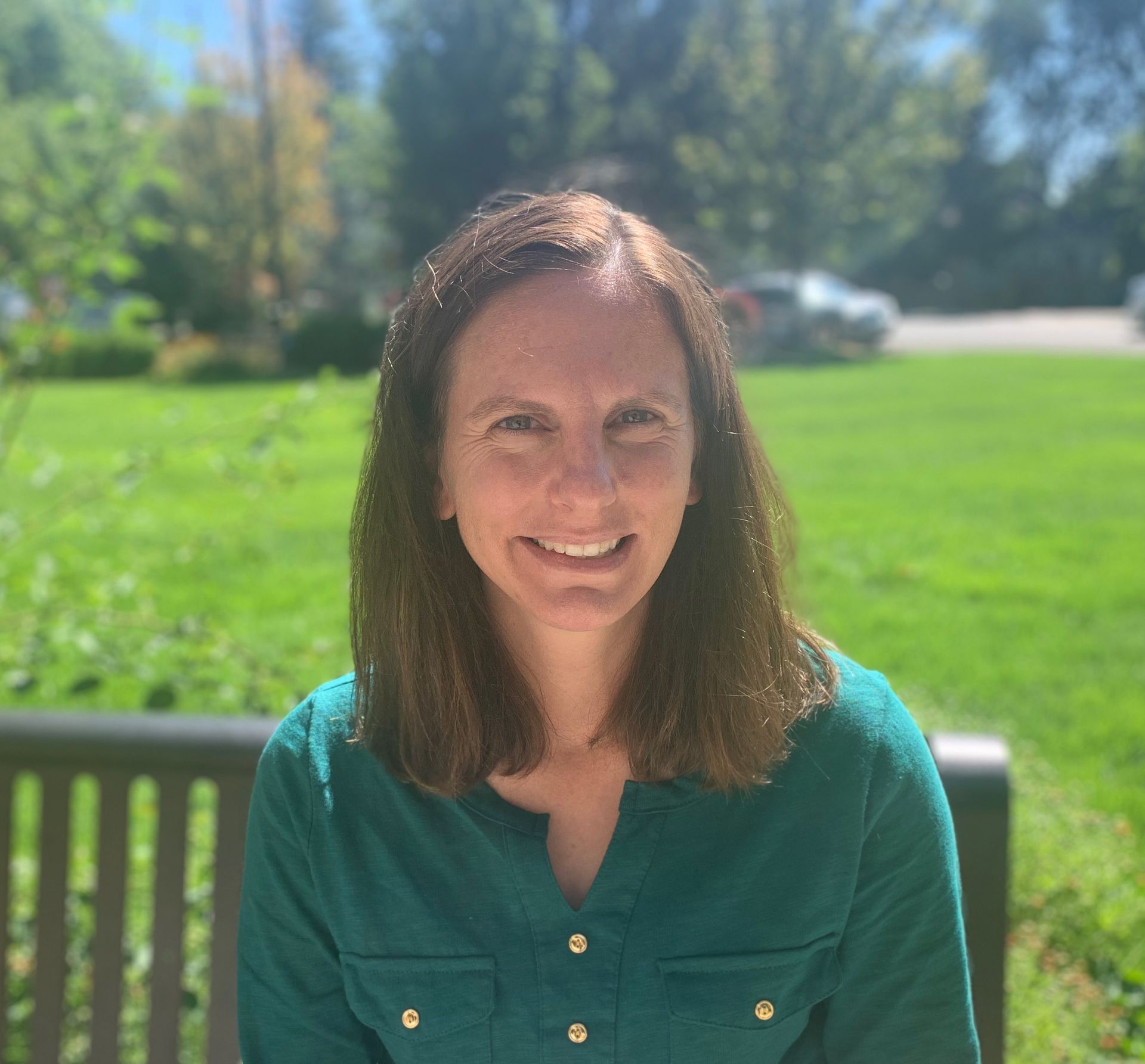 A woman is sitting on a bench in a park smiling for the camera.