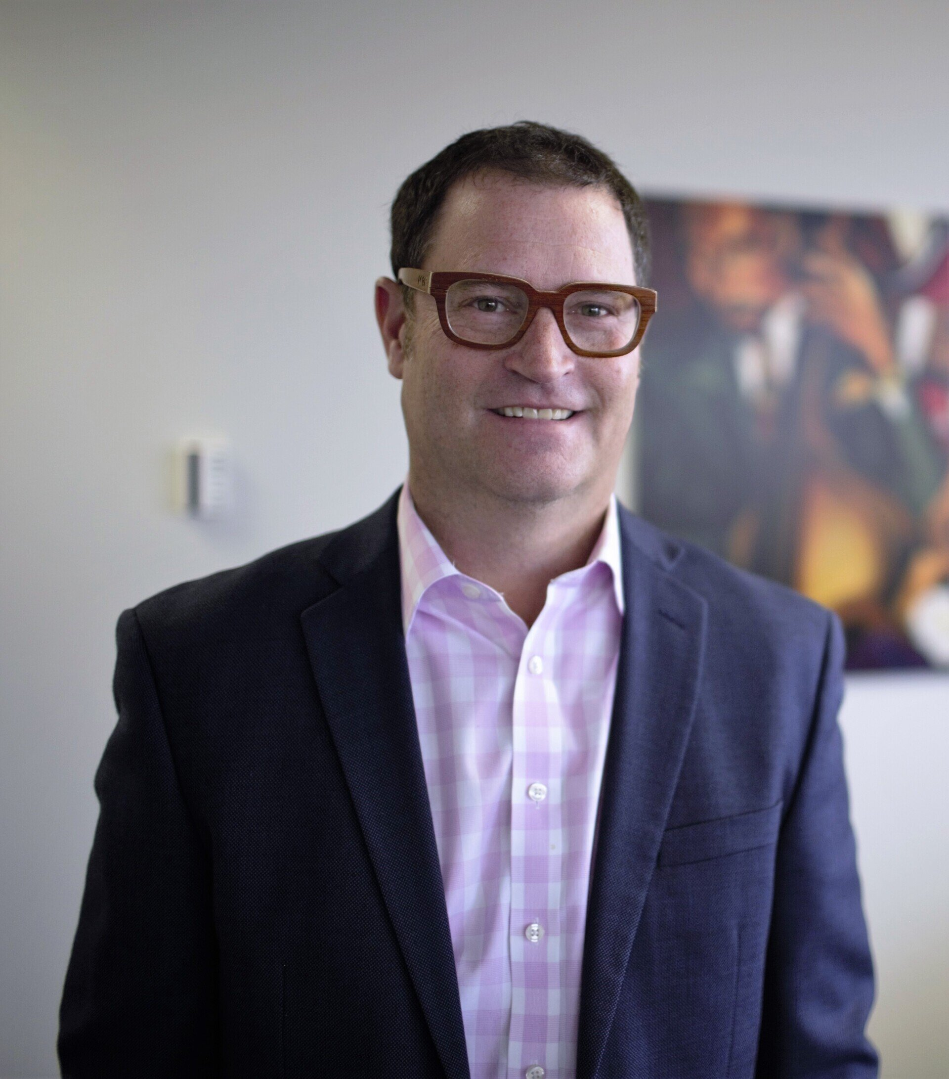 A man wearing glasses and a suit is smiling for the camera
