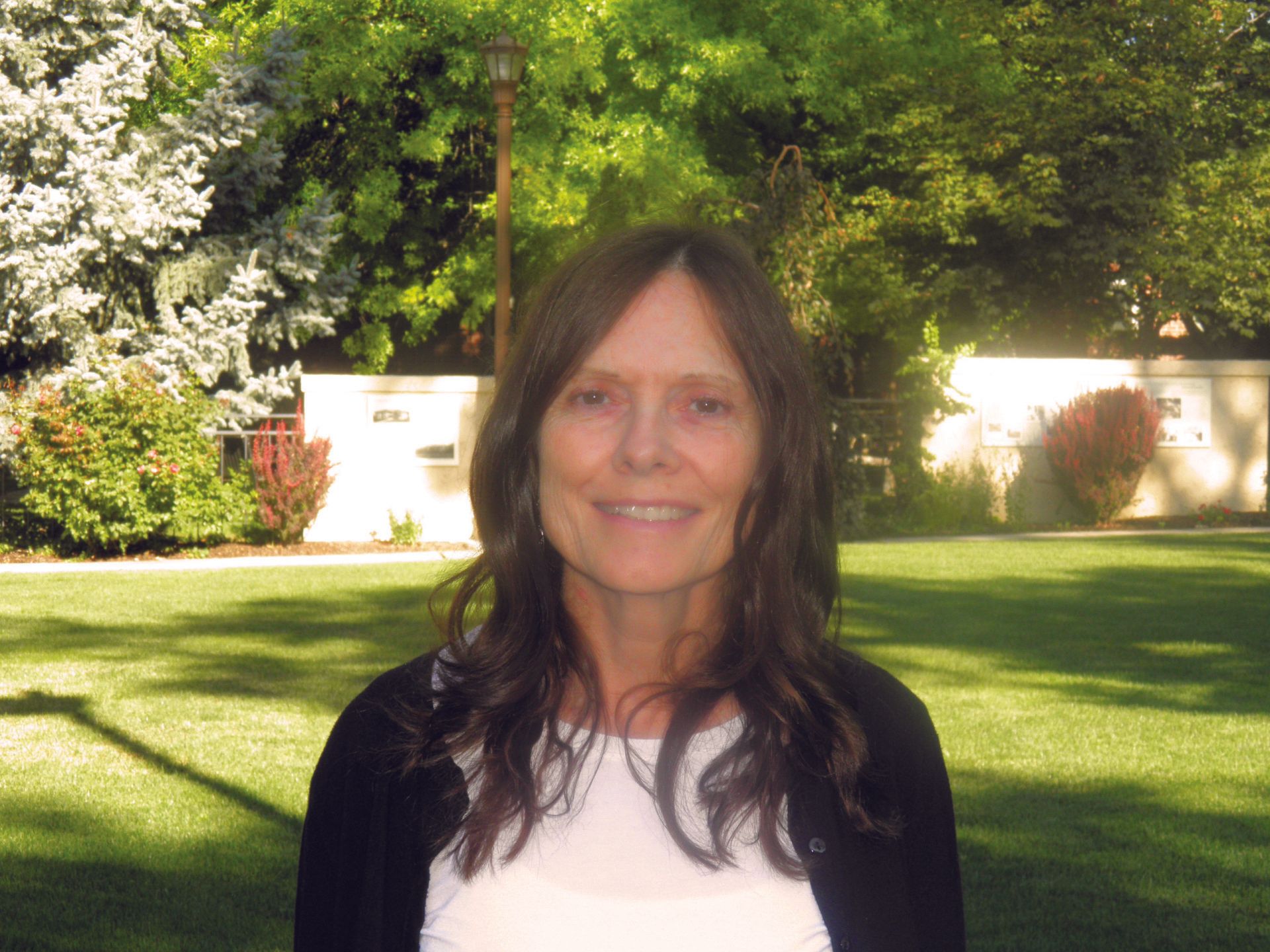 A woman in a white shirt and black cardigan is smiling for the camera