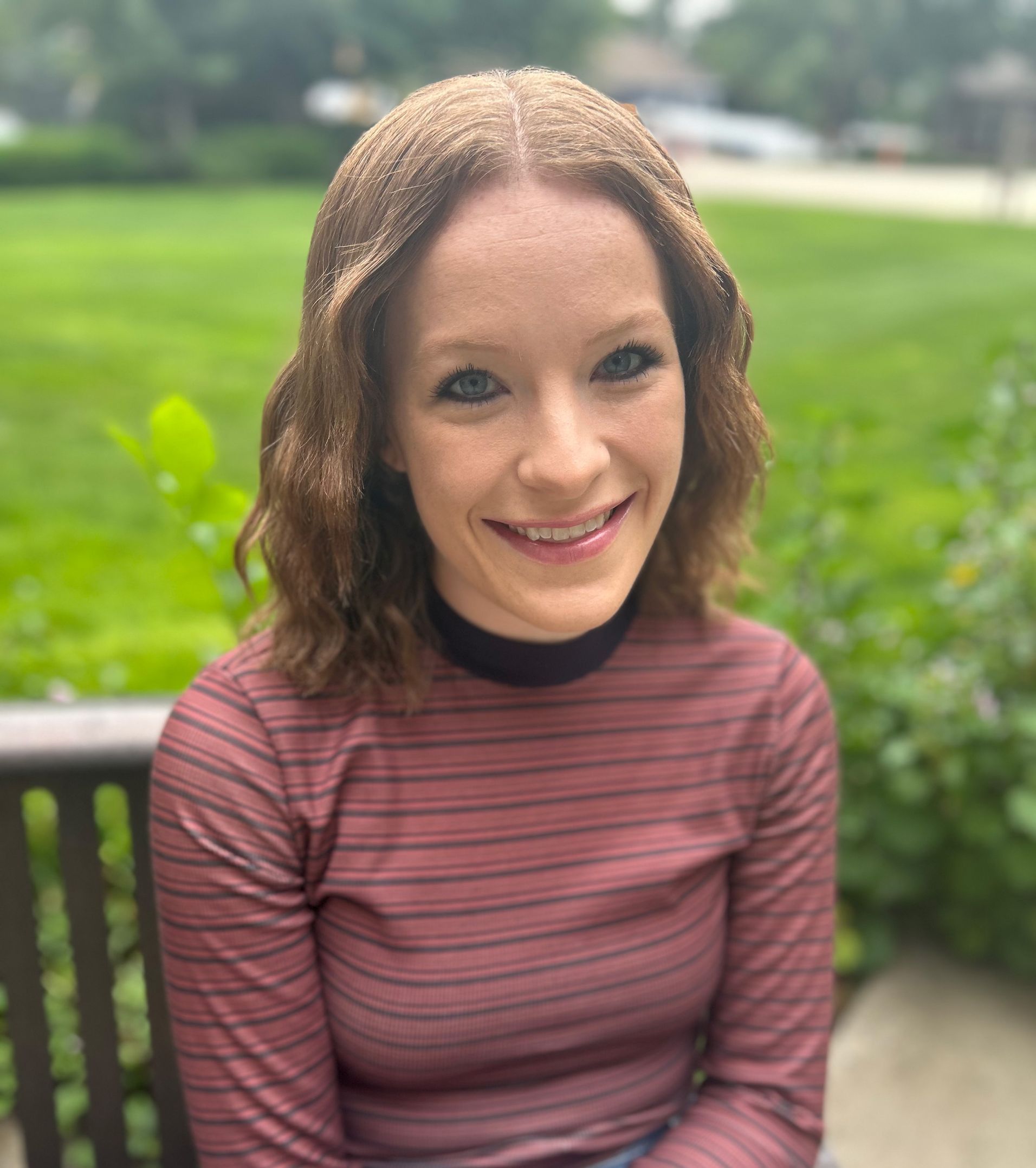 A woman is smiling while sitting on a bench in a park.