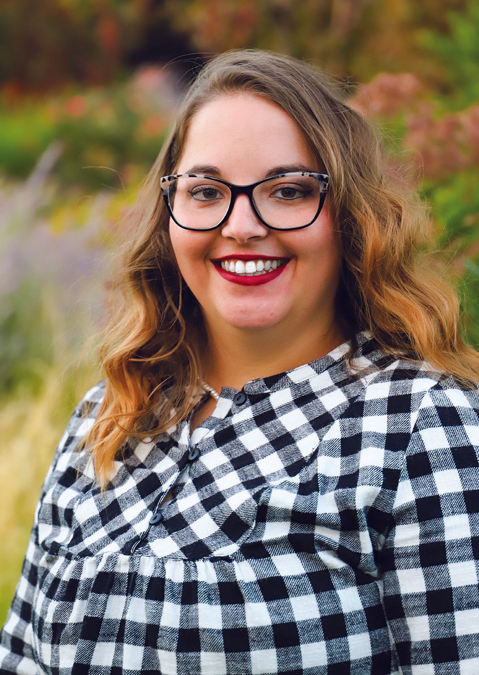 A woman wearing glasses and a plaid shirt is smiling for the camera.