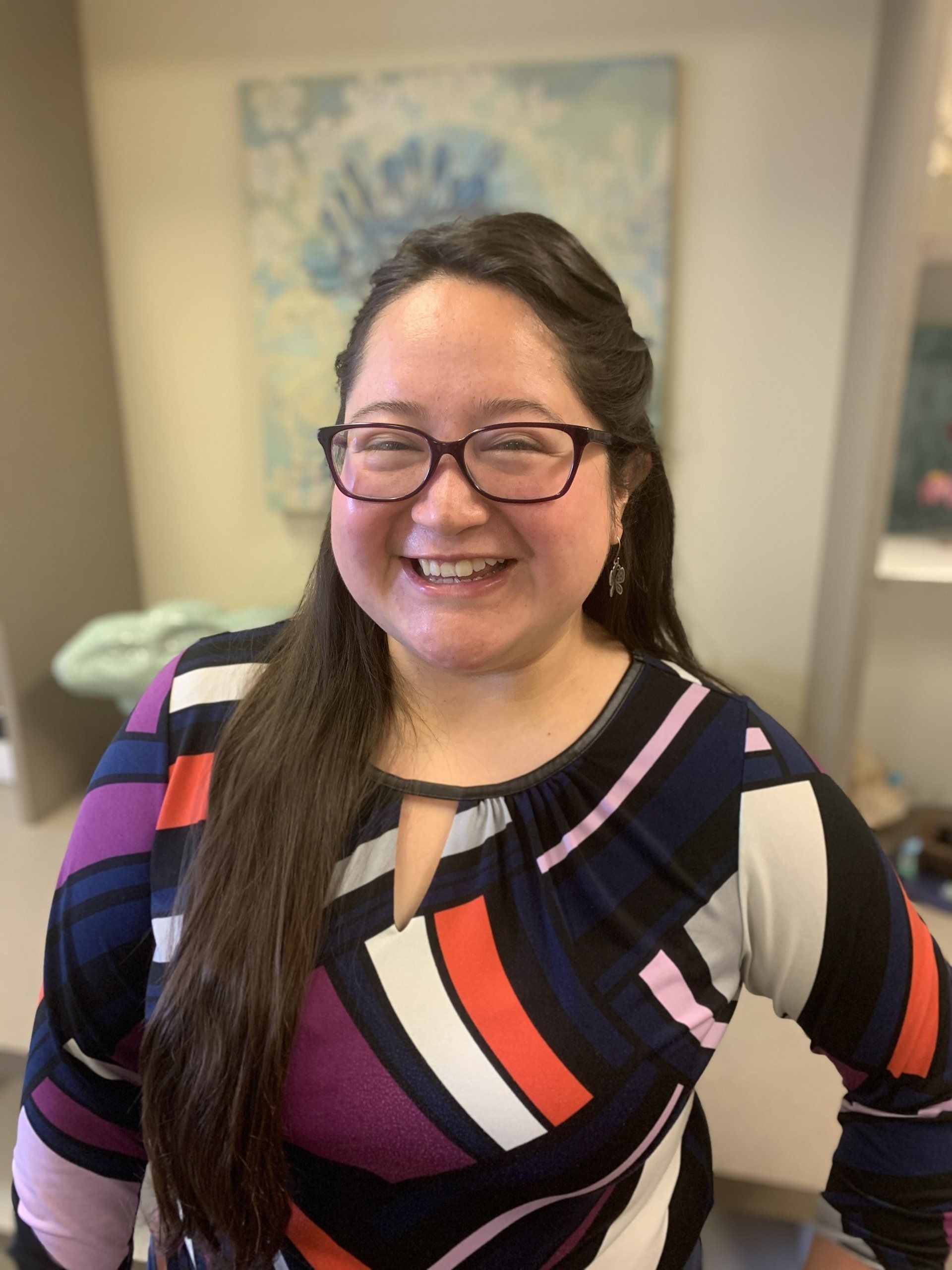 A woman wearing glasses and a colorful shirt is smiling for the camera.