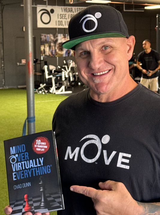 Blond woman smiling, wearing a red sweater, outdoors in front of a blurred background.