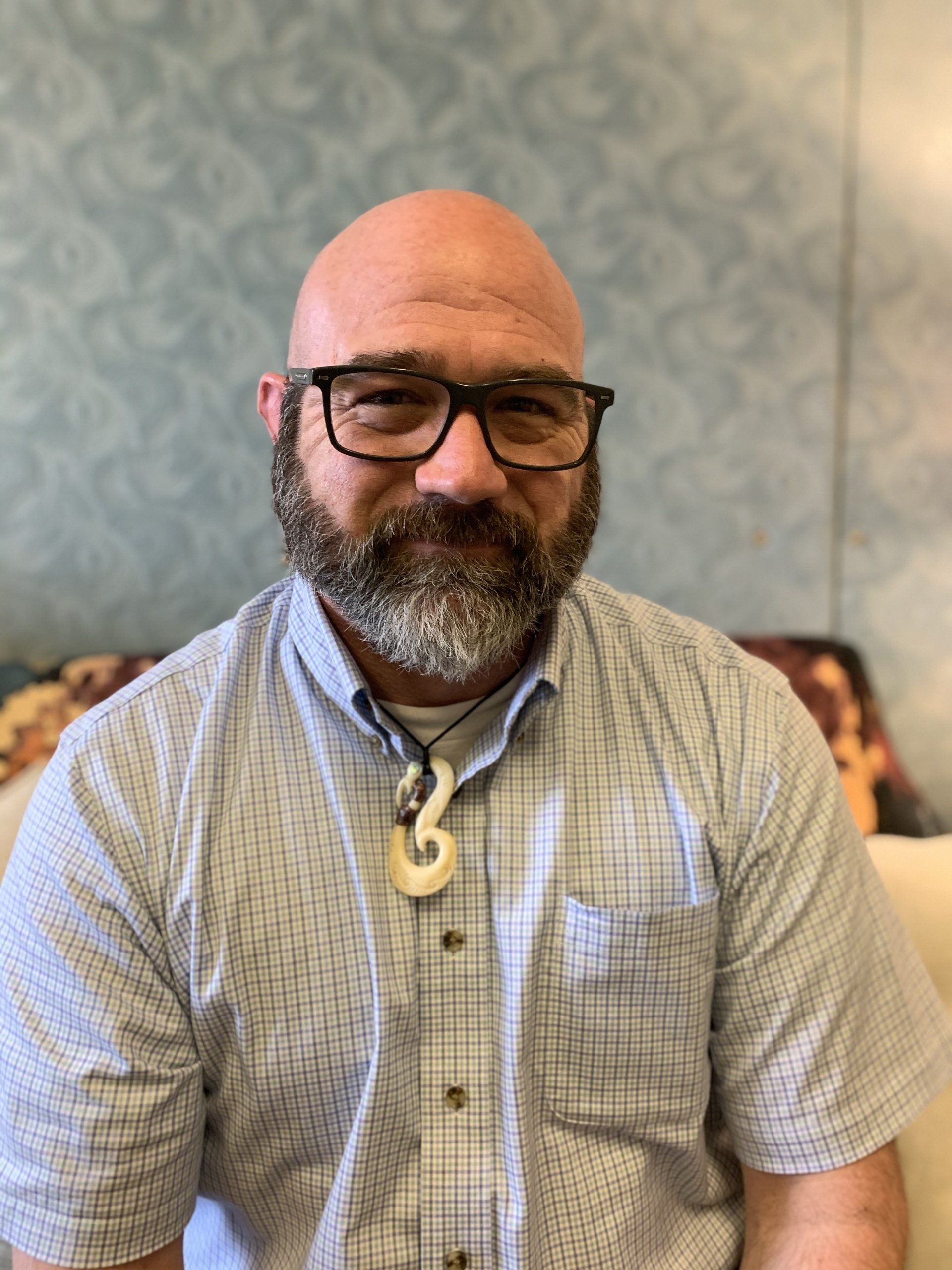 A bald man with a beard and glasses is sitting on a couch.