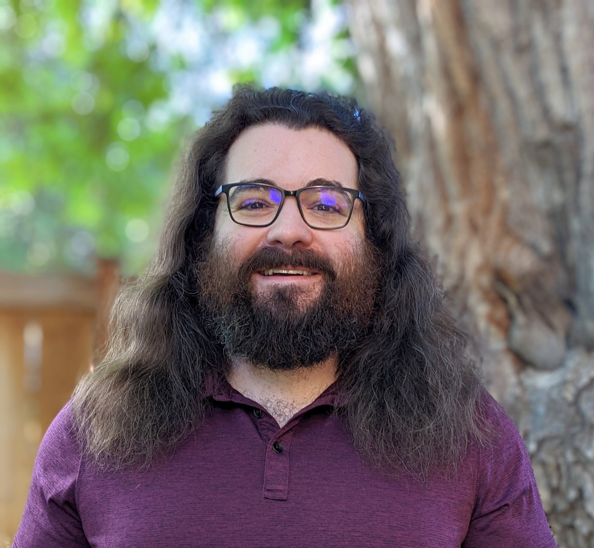 A man with long hair and a beard is wearing glasses and a purple shirt.