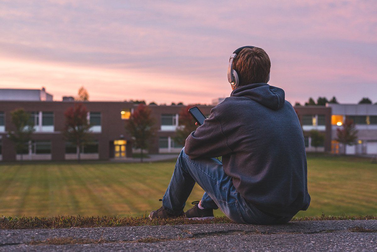 A man is sitting on the ground wearing headphones and looking at his phone.
