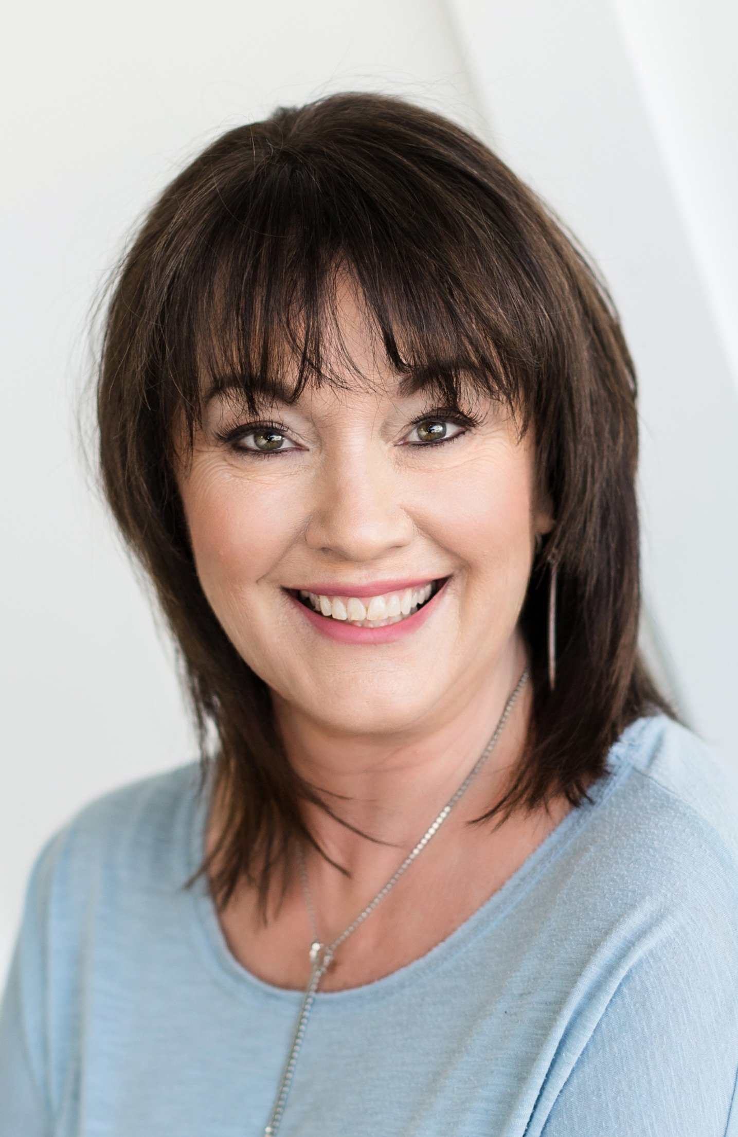 A woman wearing a blue shirt and a necklace is smiling for the camera.