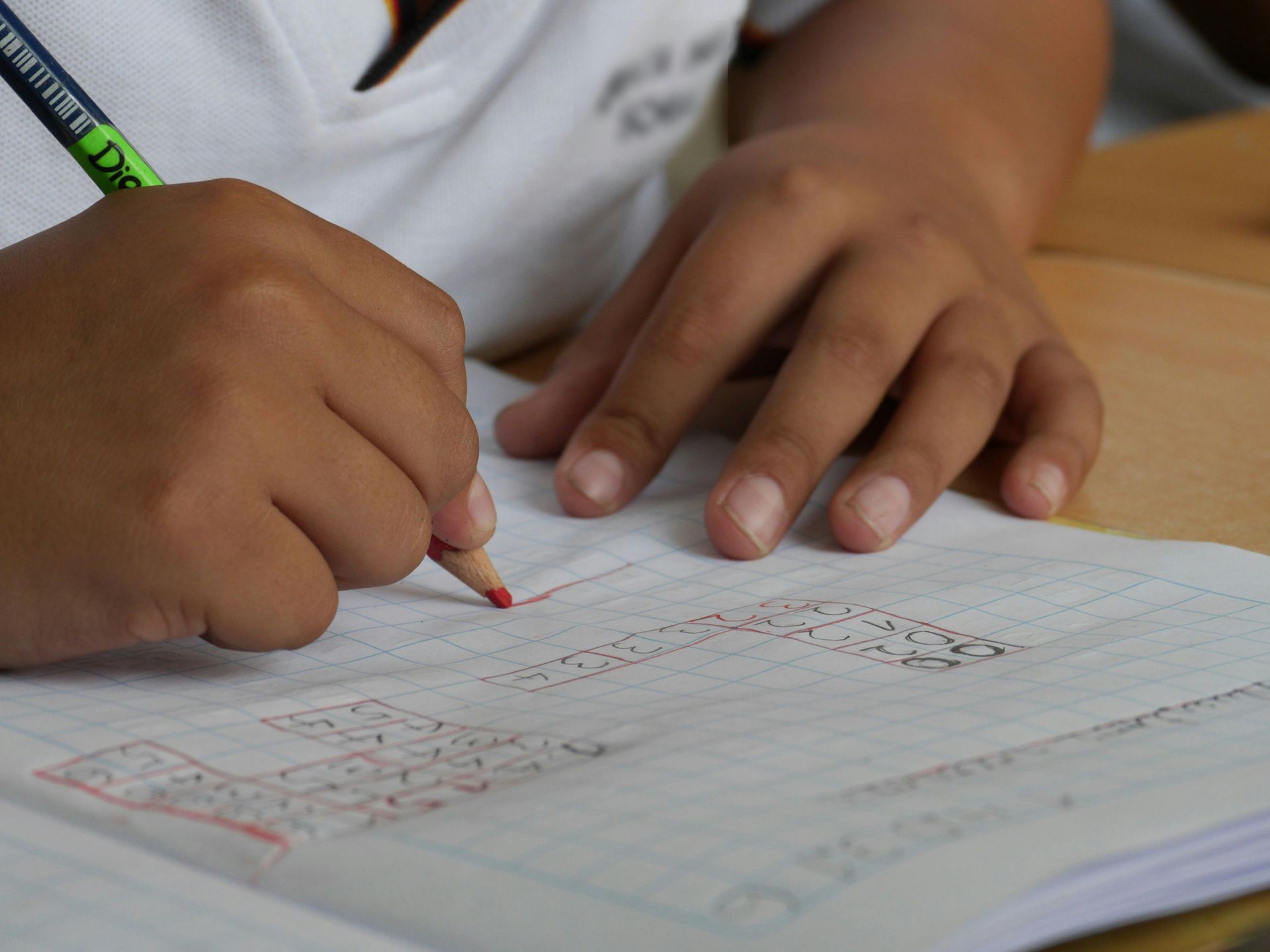 Child's hands drawing with a red pencil on graph paper, close-up shot.