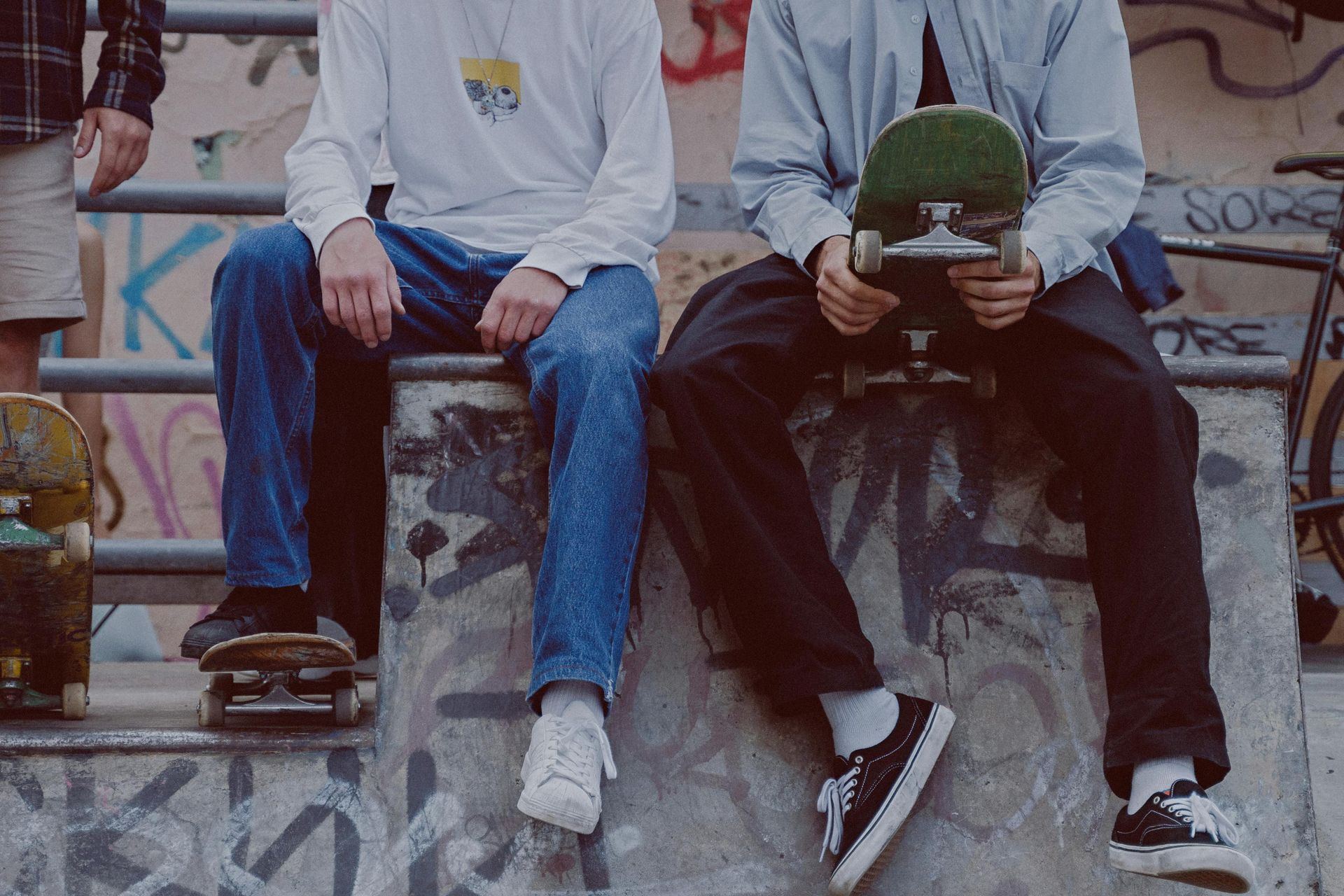 Three people sit on a concrete ledge at a skatepark holding skateboards.