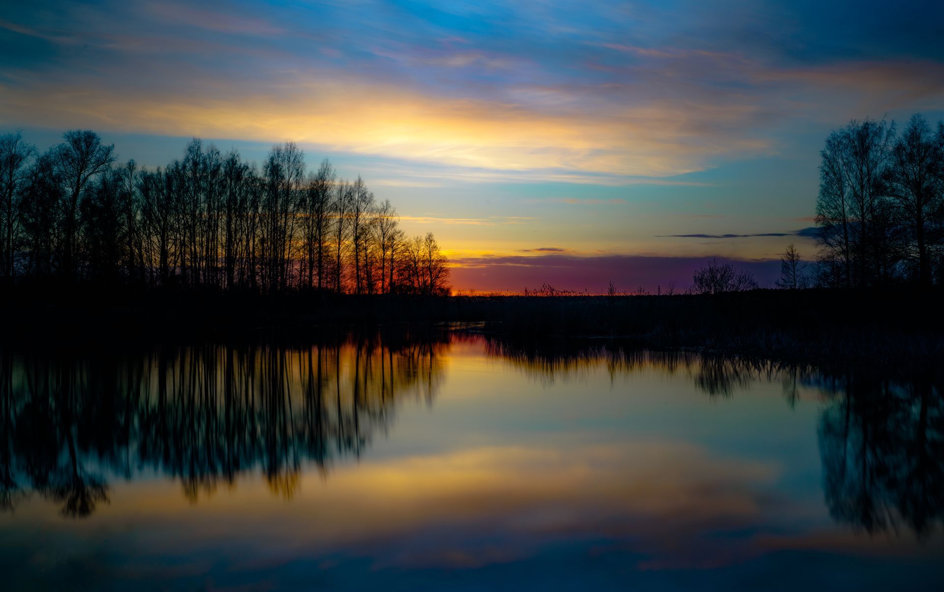 A sunset over a lake with trees silhouetted against the sky