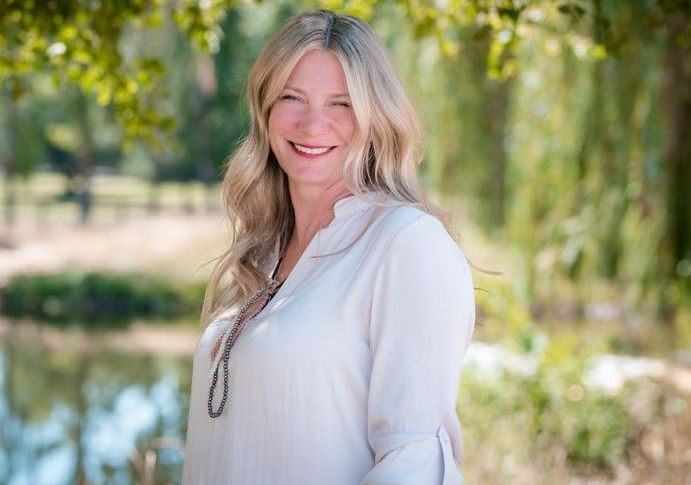 A woman in a white shirt is smiling in front of a pond.