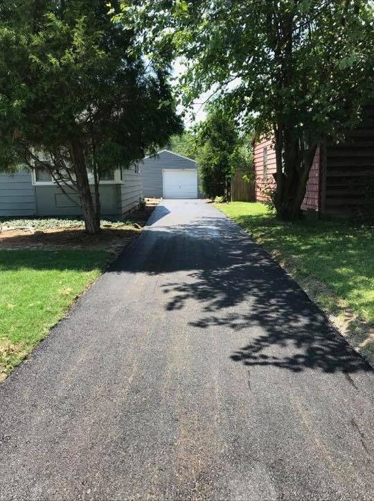 A driveway leading to a house with a garage and trees on both sides.