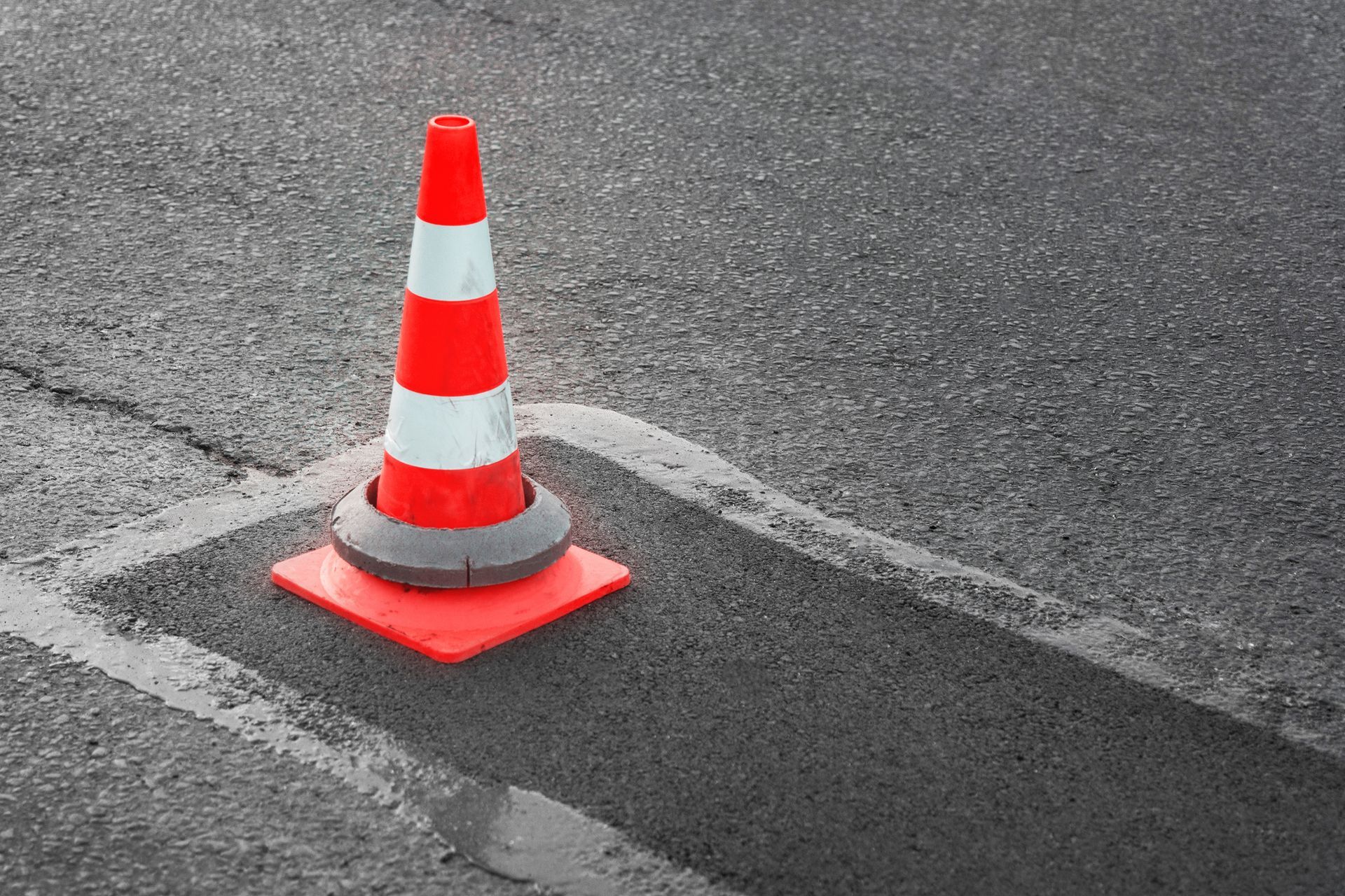 A red and white traffic cone is sitting on the side of a road.