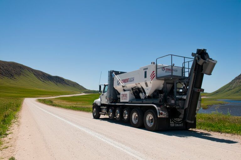 A concrete mixer truck is driving down a dirt road