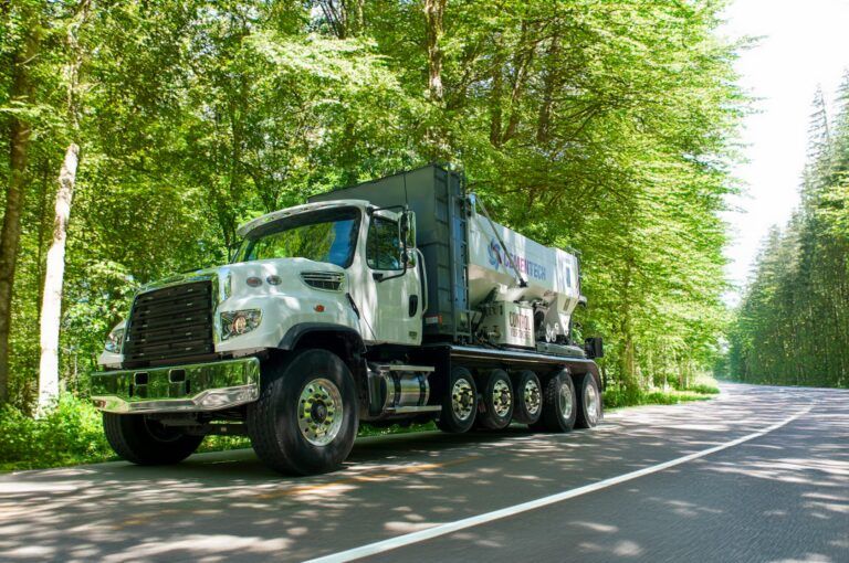A white truck is parked on the side of a road next to trees.
