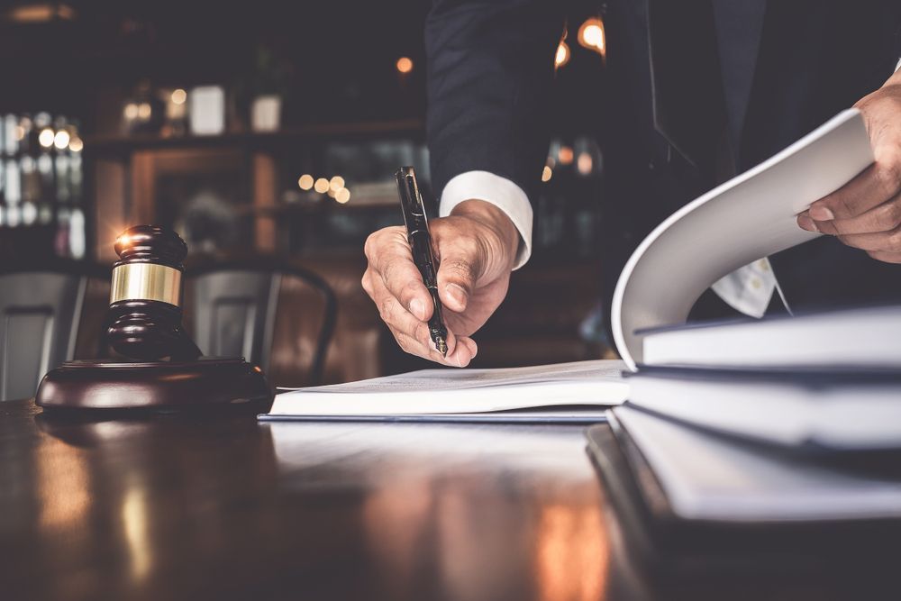 Judge signing documents beside a gavel on a desk, with legal papers in a dim office